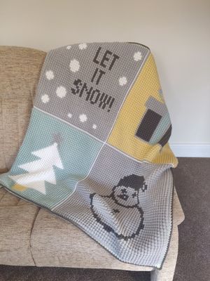 A crocheted blanket made up of 4 large squares, each with a festive design: &#39;let it snow&#39;, a present, a tree and a snowman.