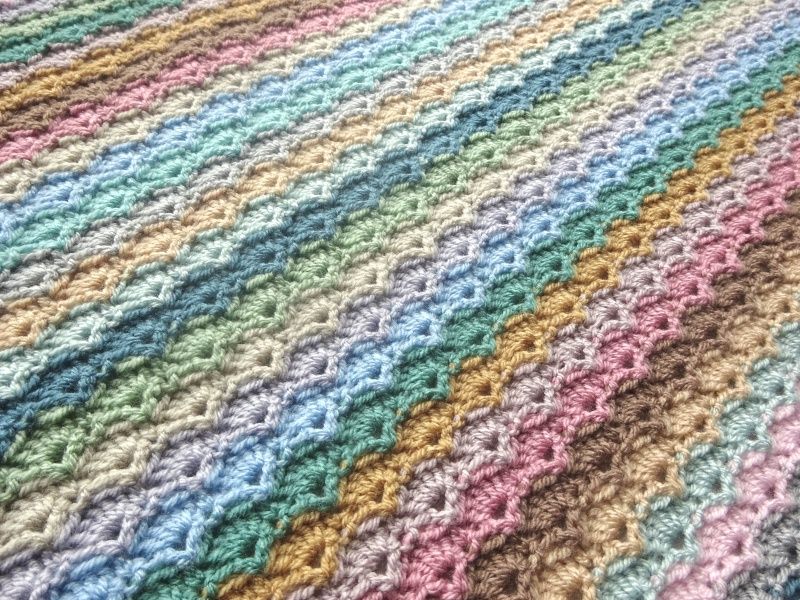 A close up of a multicoloured striped crocheted blanket in soft, pastel shades.