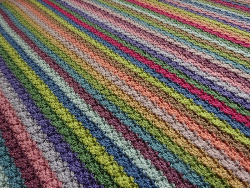A close up of a multicoloured striped crochet blanket.