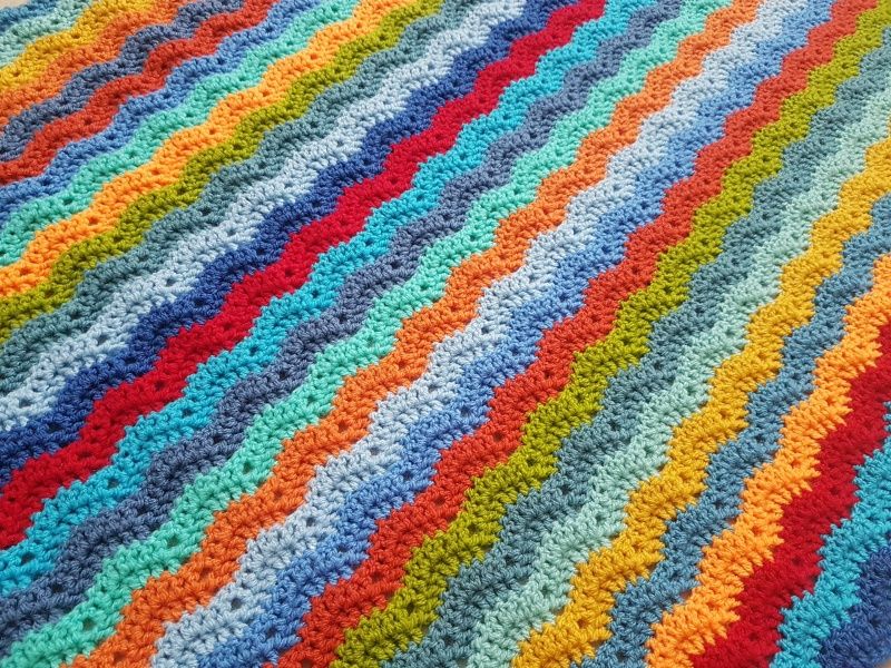 A close up of a multicoloured striped crochet blanket in bright, rainbow shades.