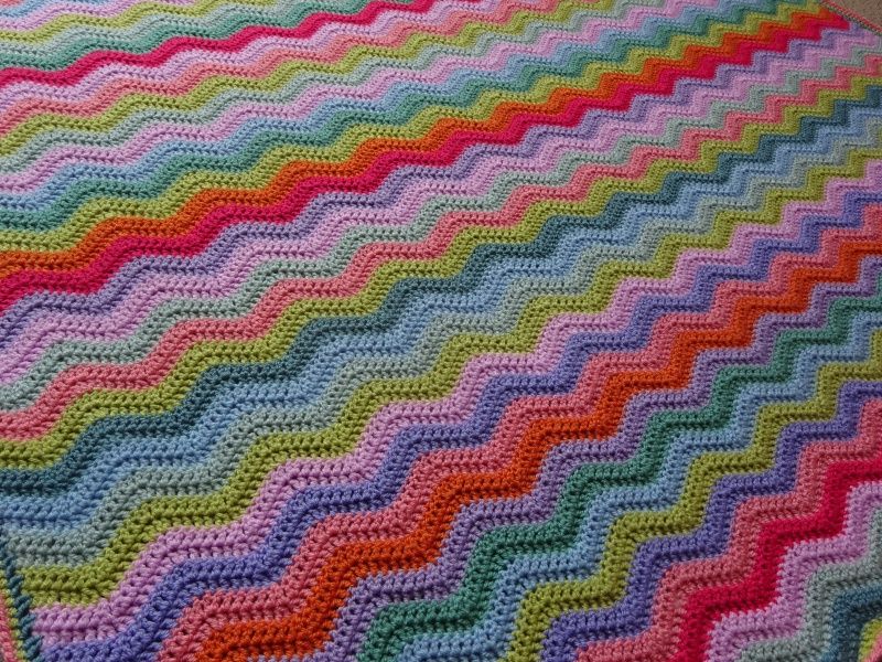 A close up of a ripple striped crochet blanket in shades of orange, green, blue, purple and pink.