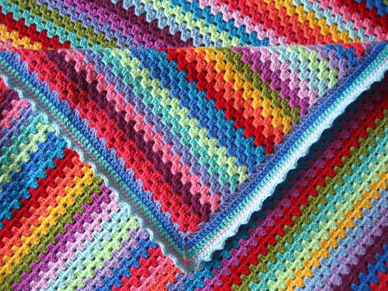 A close up of a striped crochet blanket in rainbow shades.