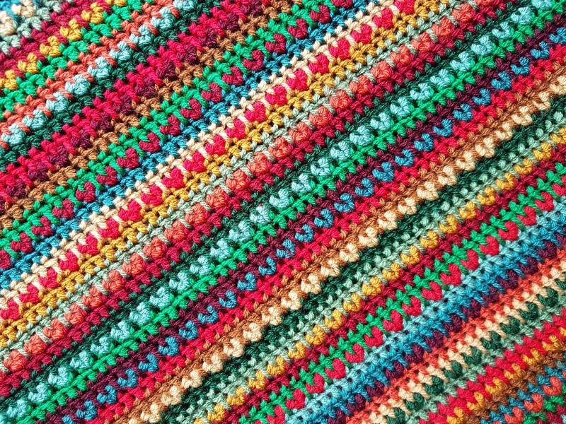 A close up of a striped crochet blanket in shades of green, red, blue and brown. 