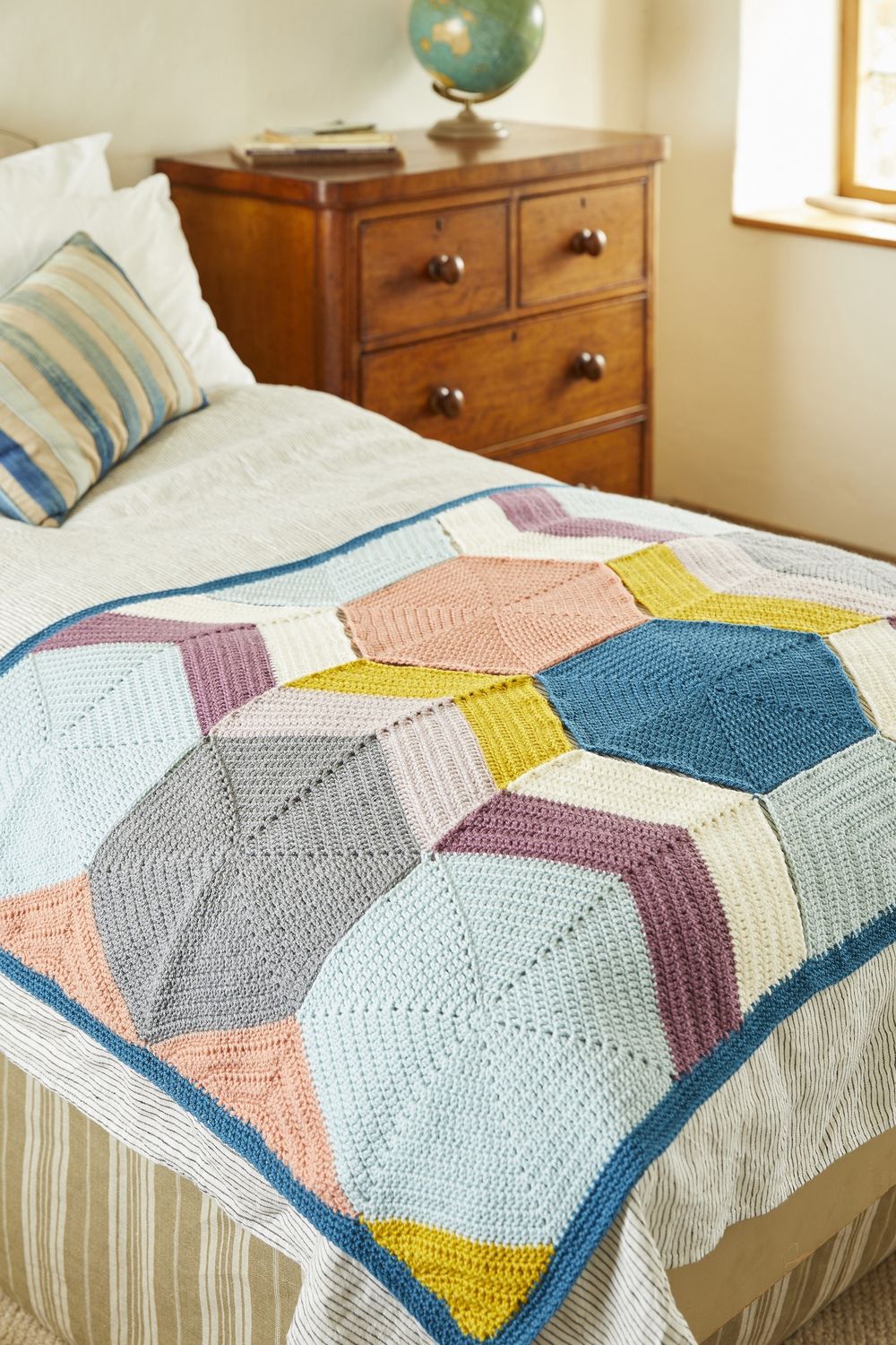 A crocheted blanket made up of hexagons in blue, purple, cream, yellow and peach.