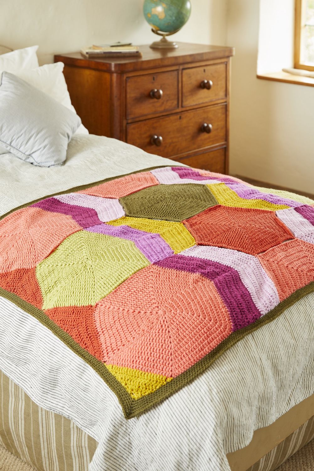A crocheted blanket made up of hexagons in green, pink, purple, yellow and peach.