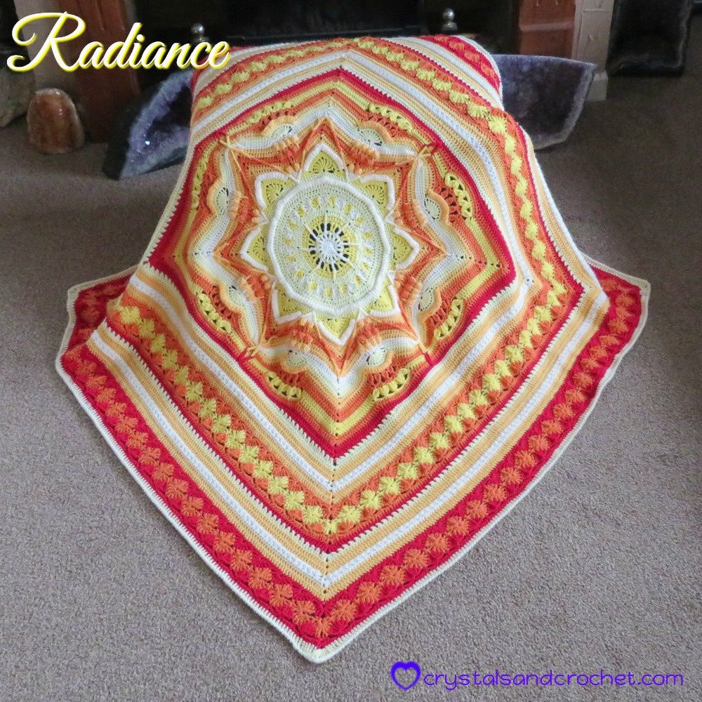 A crocheted blanket in cream, red, orange and yellow.