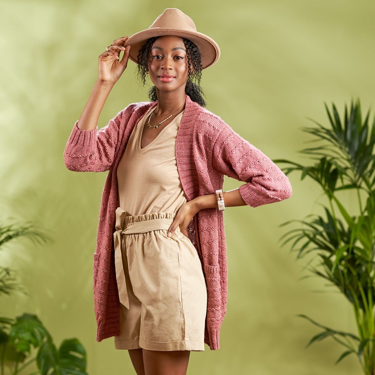 A woman is wearing a dusky pink knitted cardigan with small stripes of texture.
