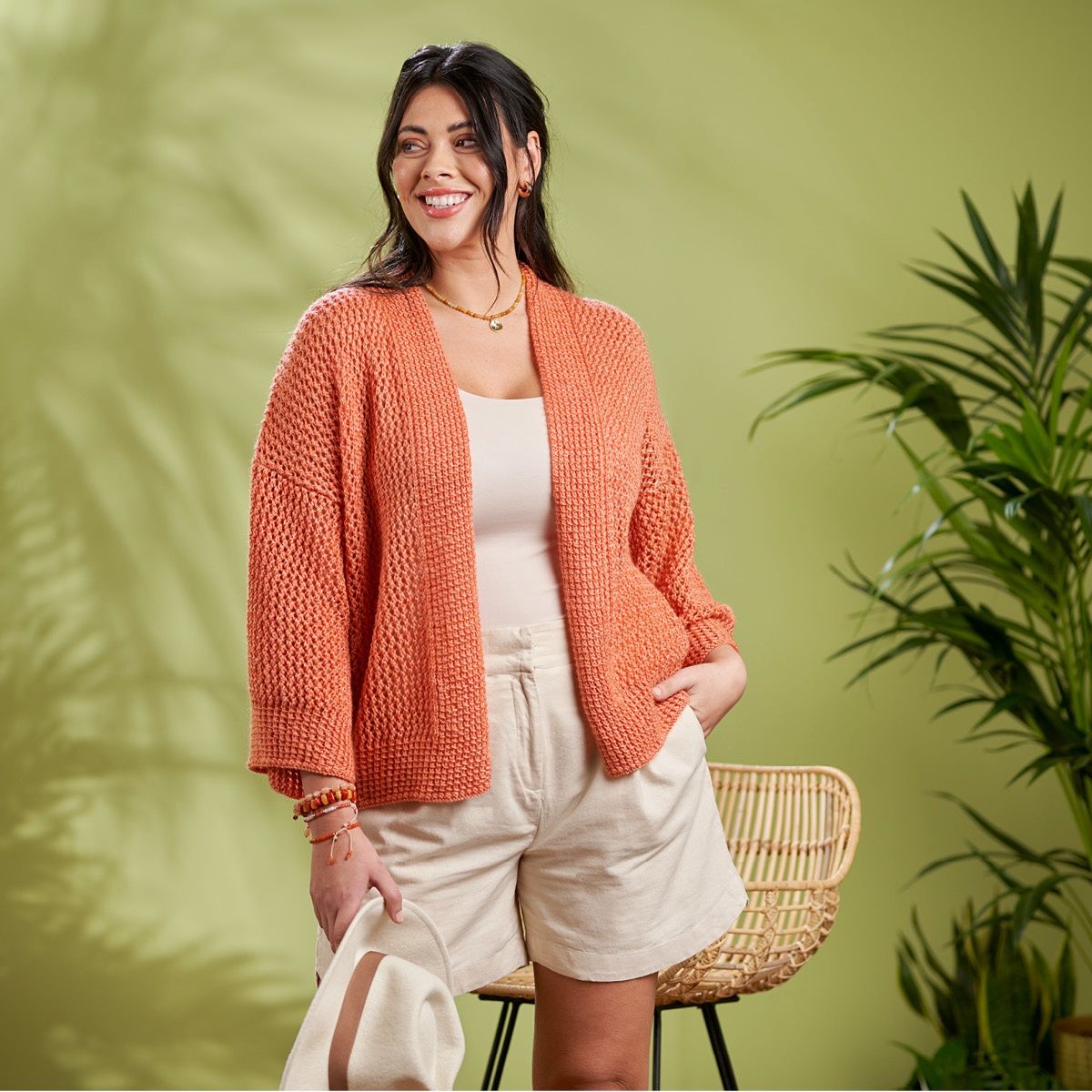 A woman is wearing a loose fitting coral orange knitted cardigan.