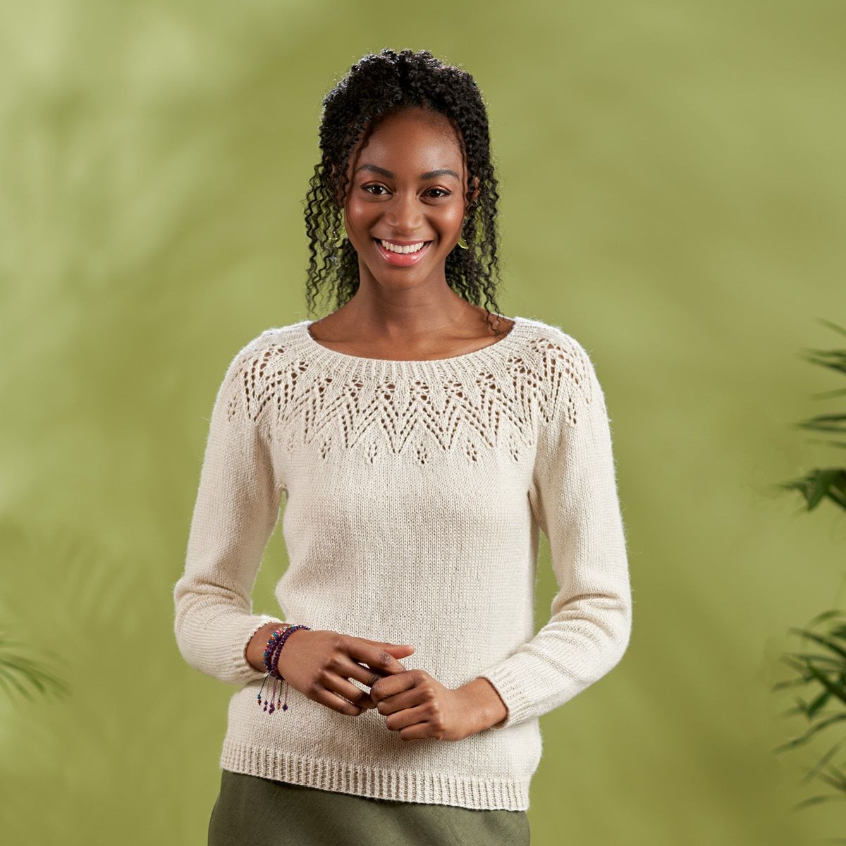 A woman is wearing a cream knitted sweater with zig zag lace detail around the yoke.
