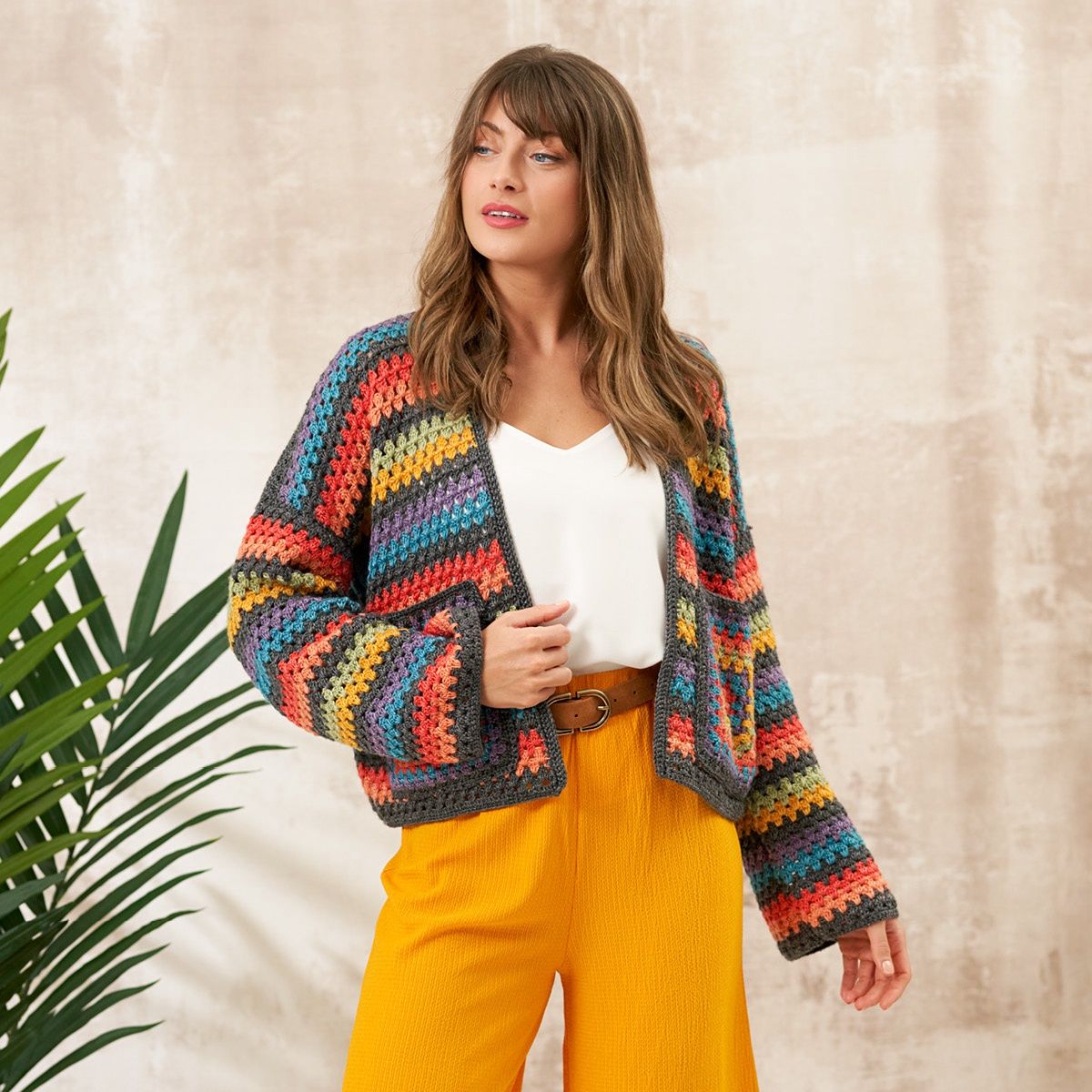 A woman is wearing a crocheted cardigan in dark grey, with red, blue, yellow, green and purple stripes.