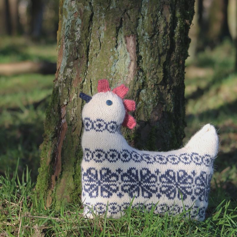 A cream knitted chicken with dark colourwork on it's body.
