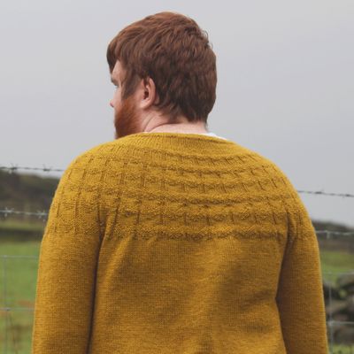 A man is wearing a yellow knitted sweater with textured stitches on the yoke.
