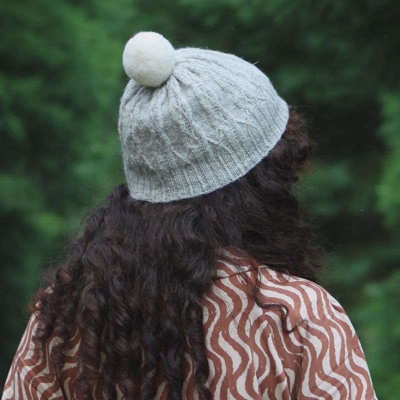A woman is wearing a cream knitted hat with cream pompom on top.