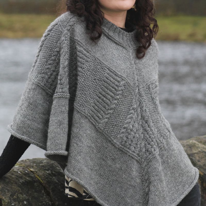 A woman is wearing a grey knitted poncho with textured sections.