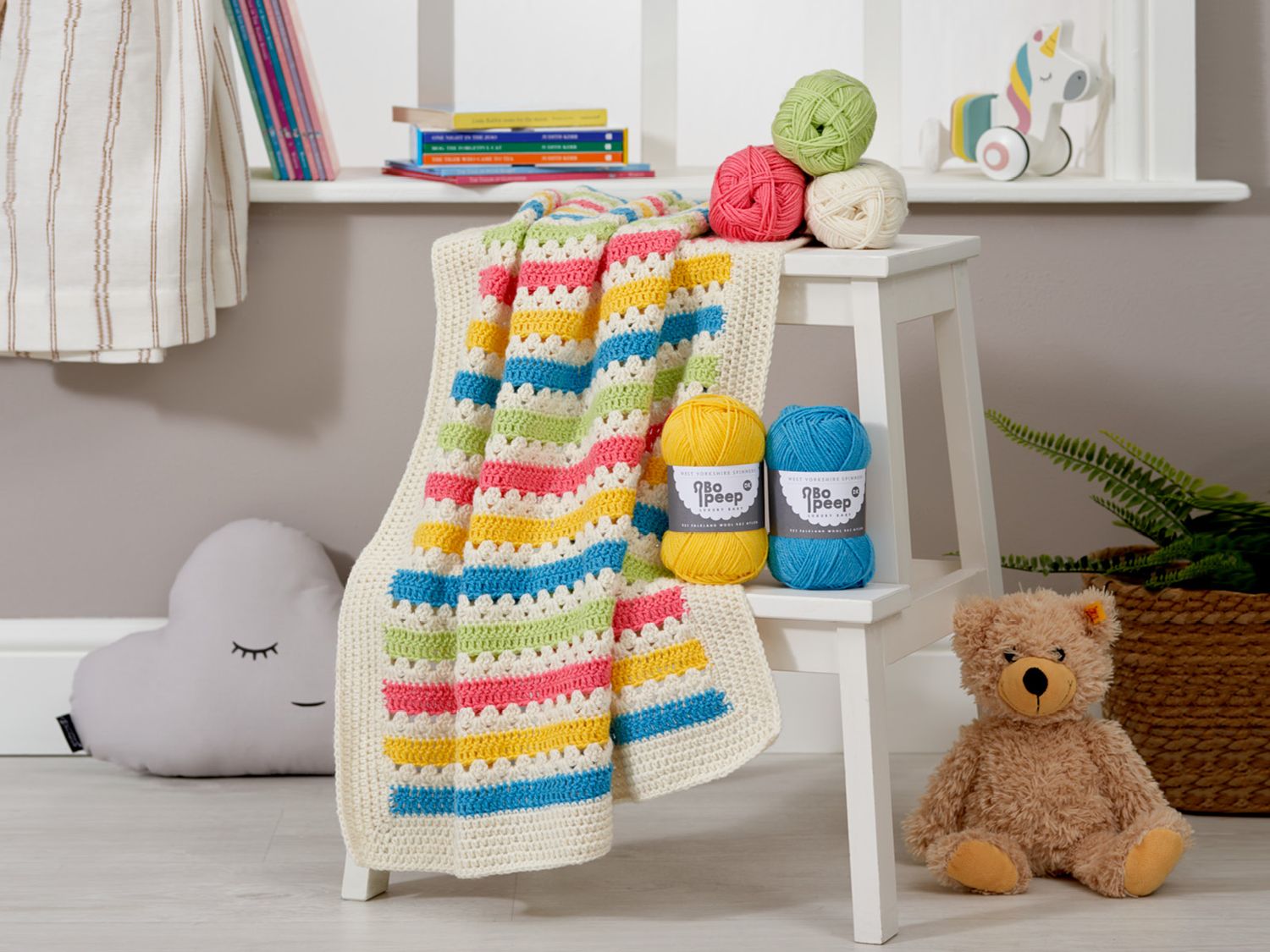 A cream, blue, red, green and yellow striped crochet blanket.