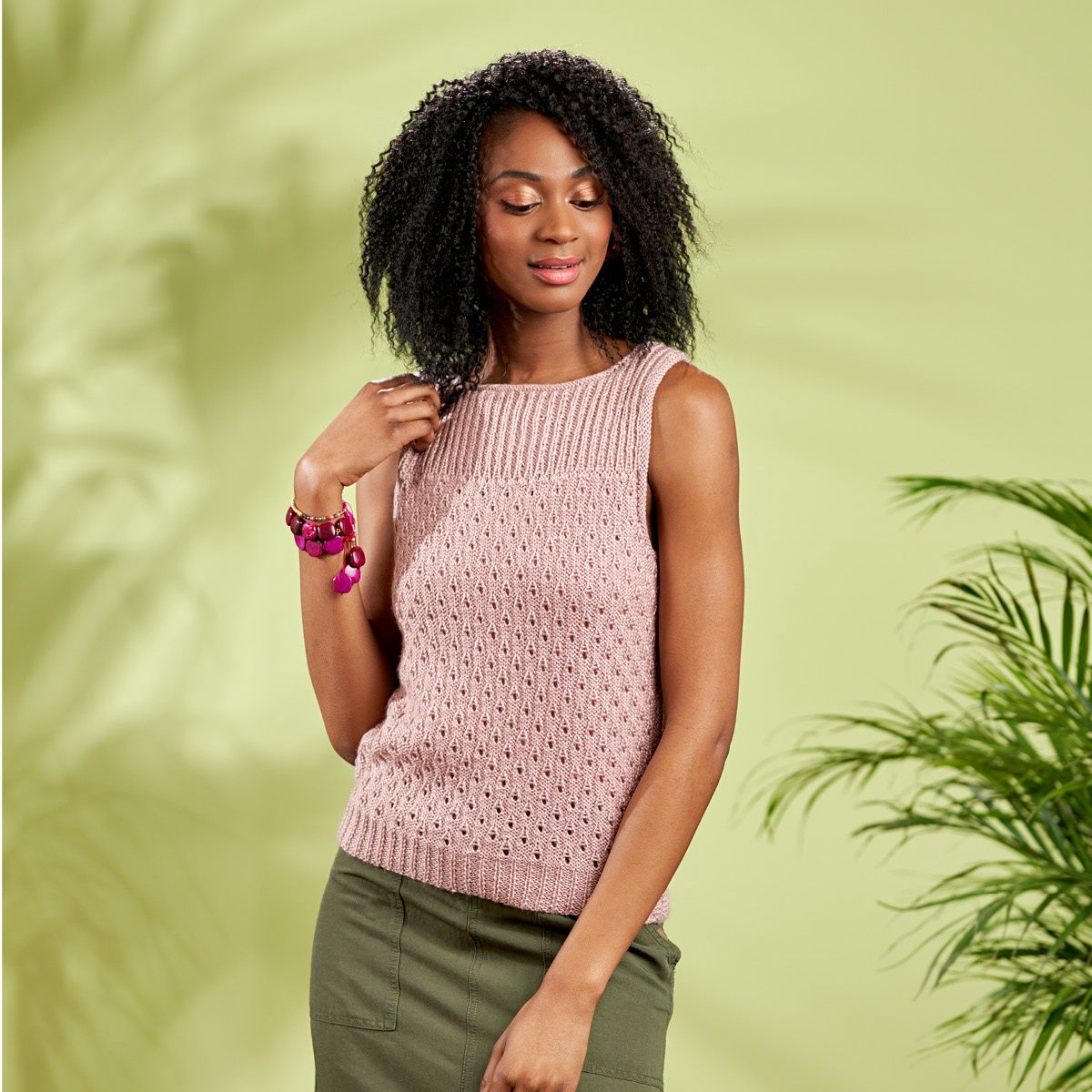 A woman is wearing a light pink lacy knitted tank top.
