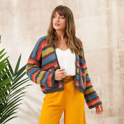 A woman is wearing a crocheted cardigan in dark grey, with red, blue, yellow, green and purple stripes.