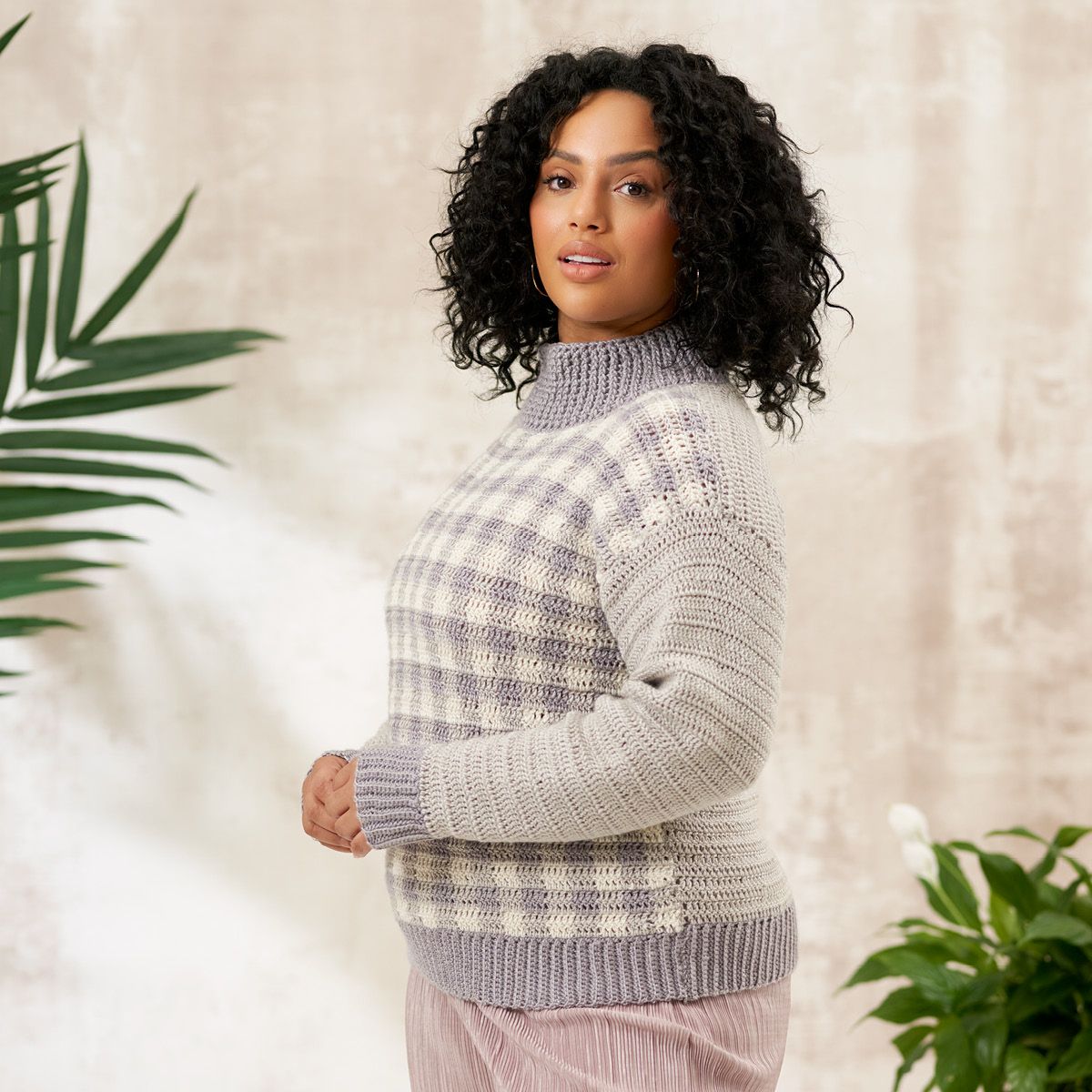 A woman is wearing a pale grey and purple crocheted jumper, with a checked pattern on the front.