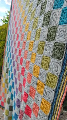 A crocheted blanket made up of silver and rainbow squares.