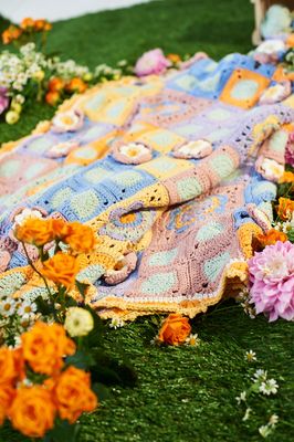 A crocheted blanket, made up of blue, yellow, purple and pink floral squares.