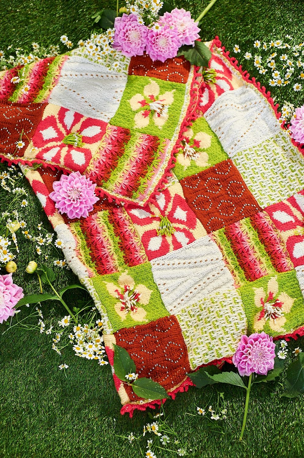 A knitted blanket made up of red, white and green floral and textured squares.