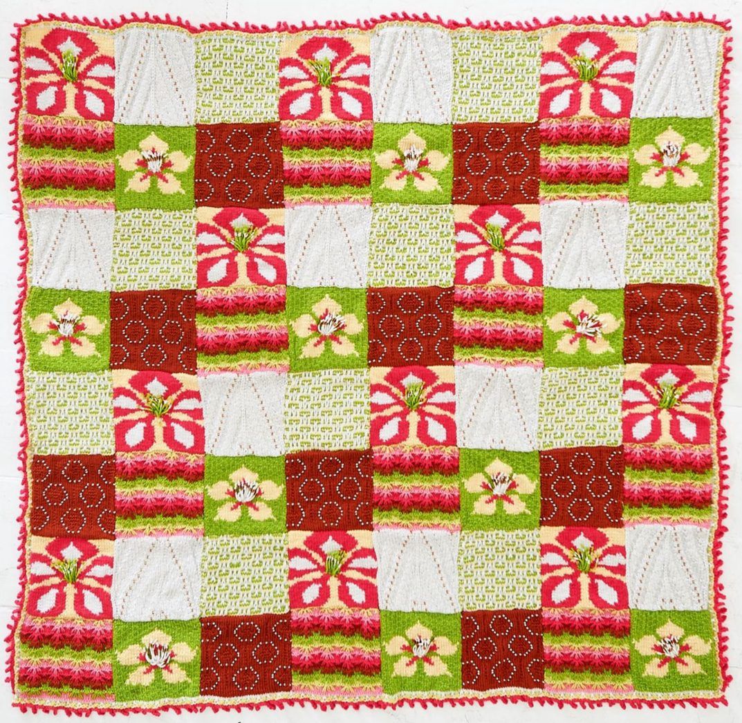 A knitted blanket made up of red, white and green floral and textured squares.