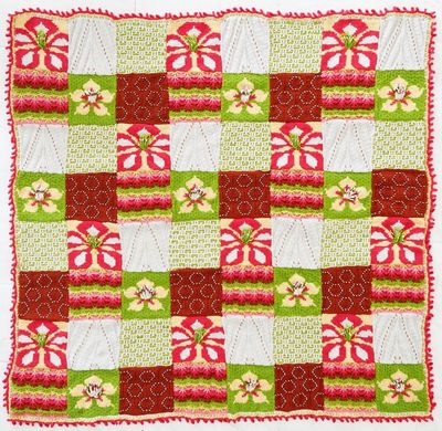 A knitted blanket made up of red, white and green floral and textured squares.