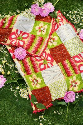 A knitted blanket made up of red, white and green floral and textured squares.