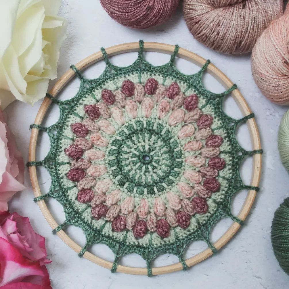 A crocheted mandala in shades of green and pink.