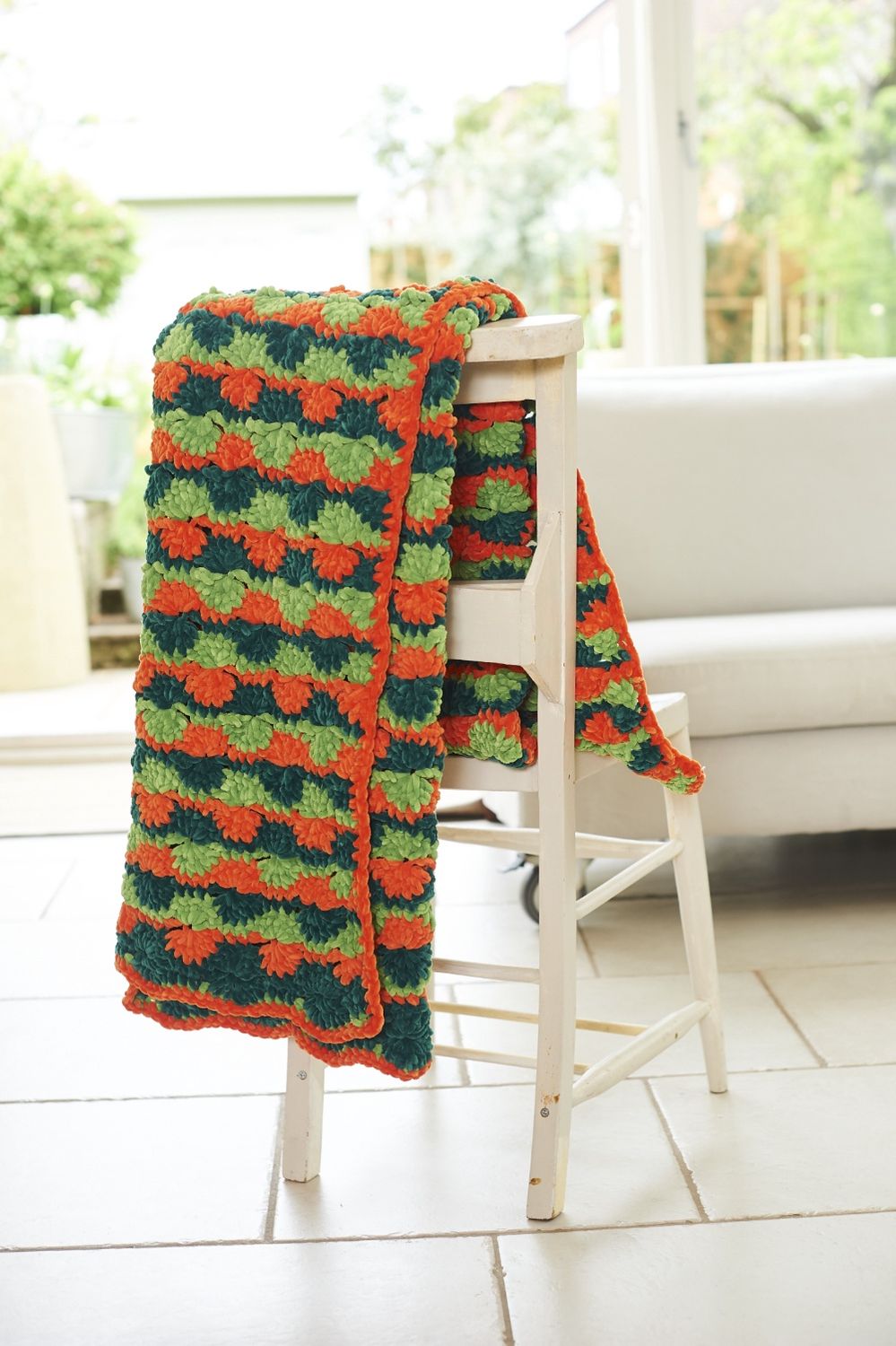 A crocheted blanket in orange, light green and dark green.