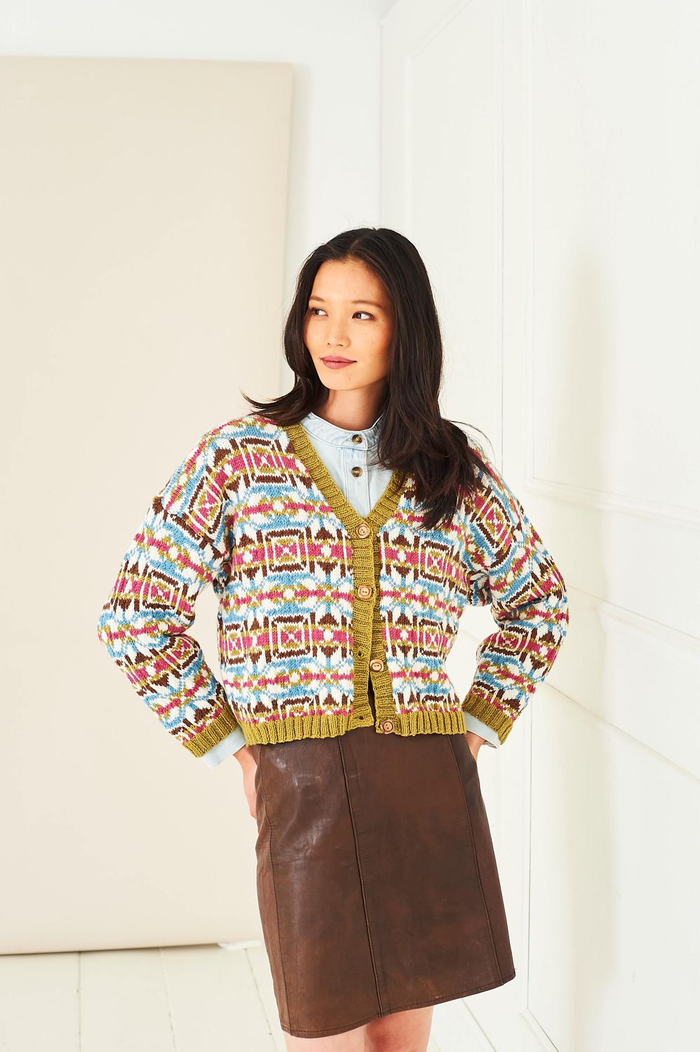 A woman is wearing a knitted colourwork cardigan, in cream, blue, green and reds.