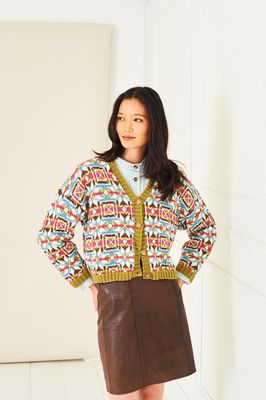 A woman is wearing a knitted colourwork cardigan, in cream, blue, green and reds.