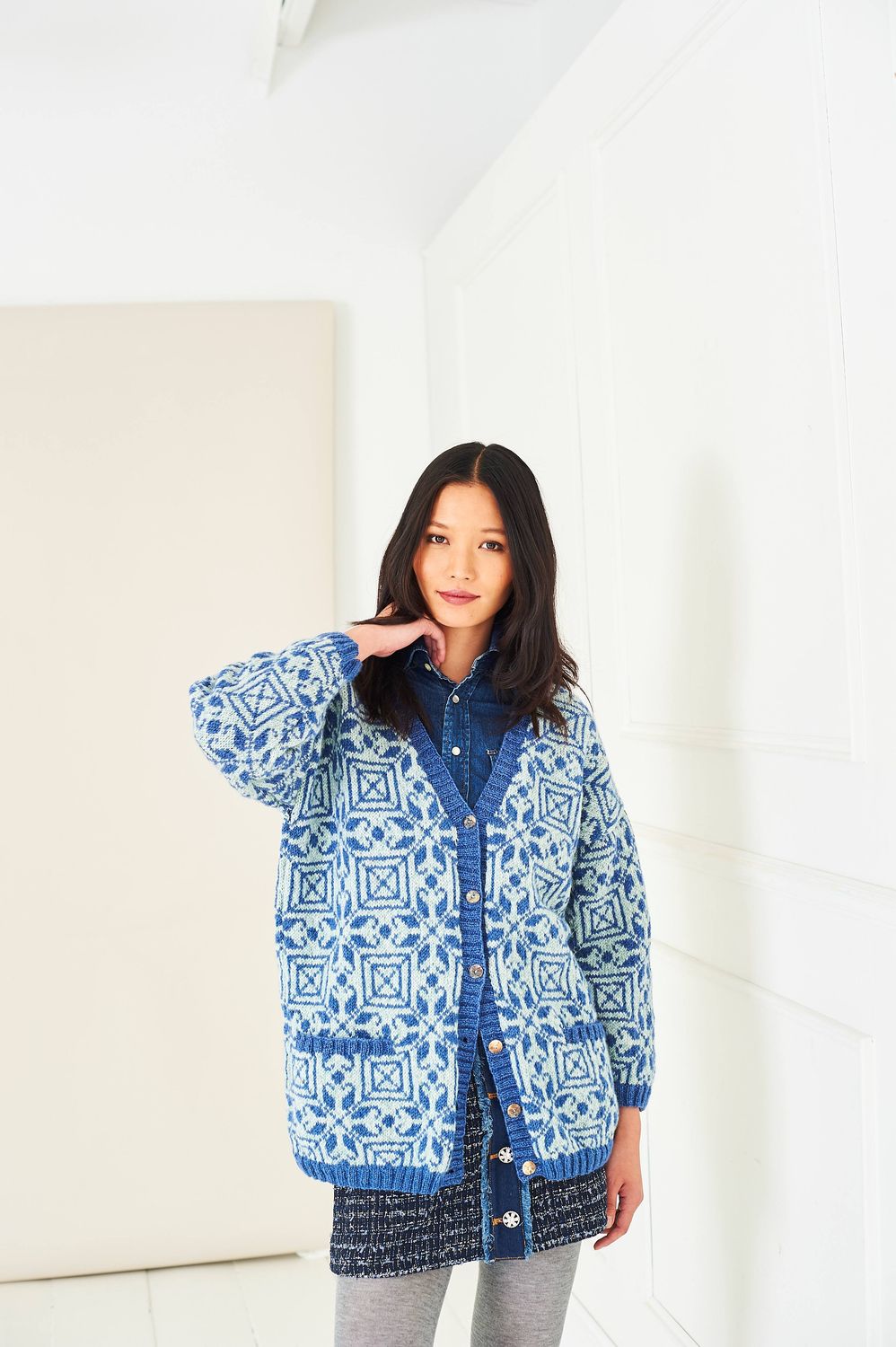 A woman is wearing a knitted colourwork cardigan, in cream and blues.