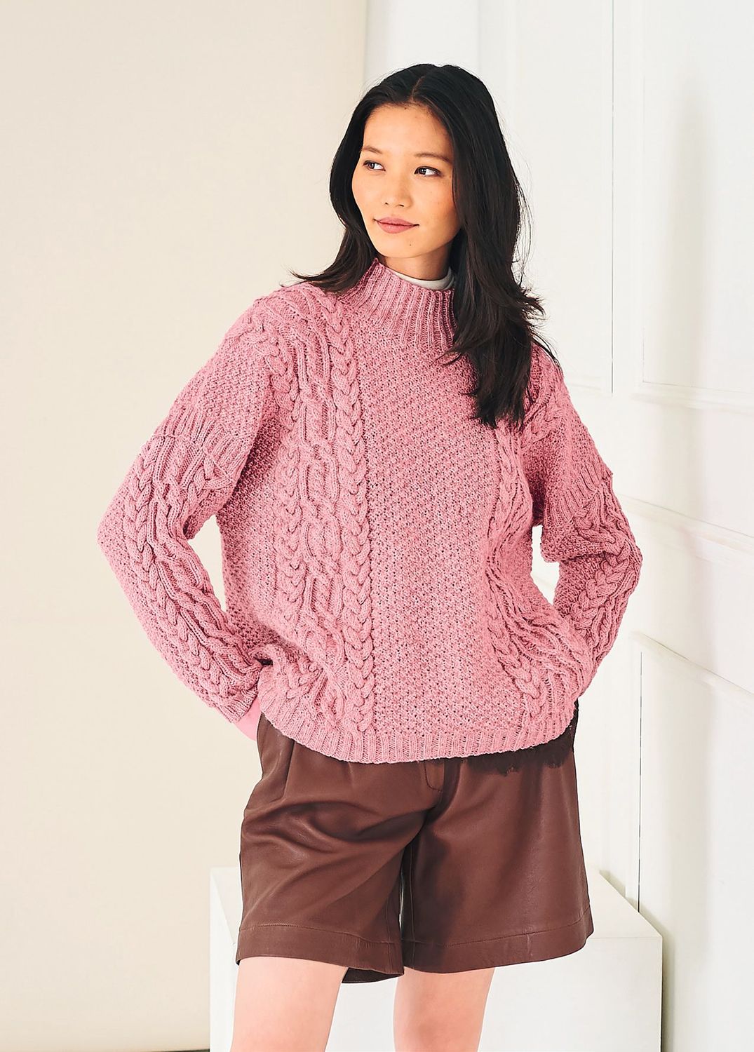 A woman is wearing a pink cable knit sweater.