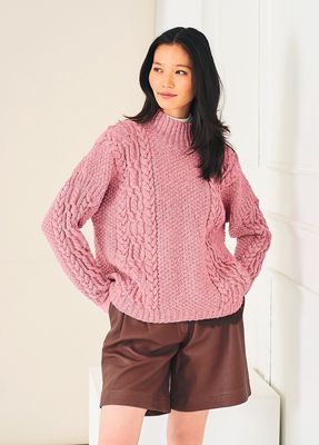 A woman is wearing a pink cable knit sweater.