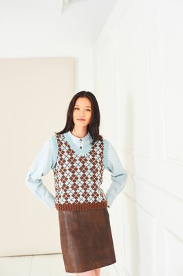 A woman is wearing a blue and brown fair isle knitted tank top.