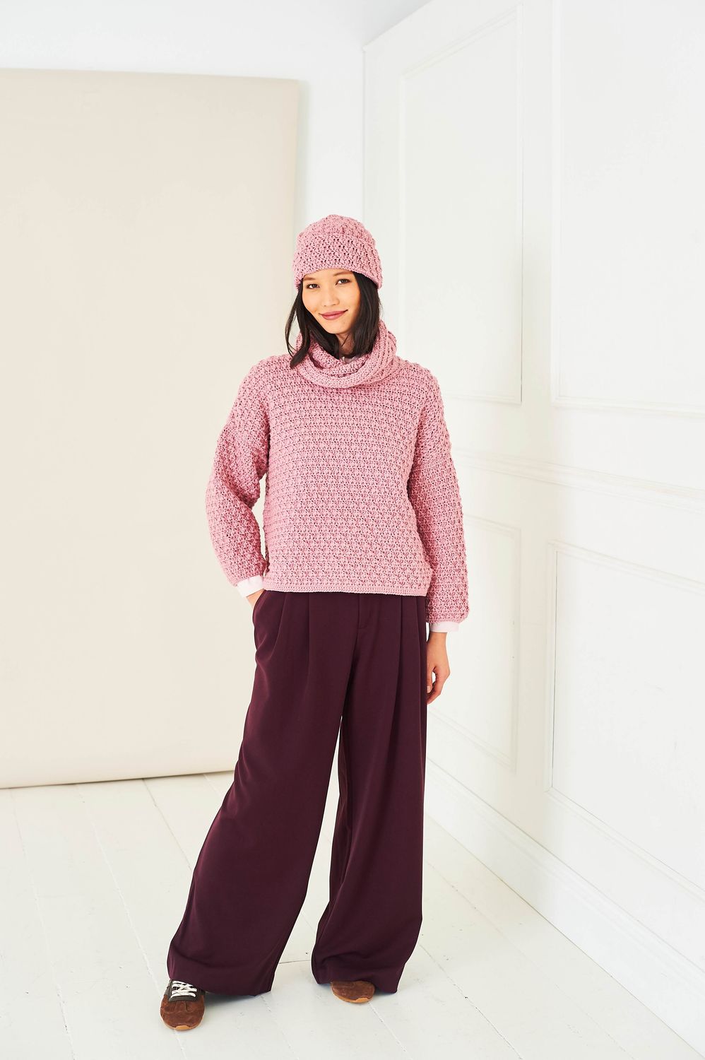 A woman is wearing a pink crocheted sweater and hat.