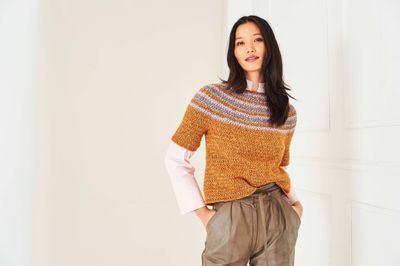A woman is wearing a brown crocheted top with a colourwork yoke.
