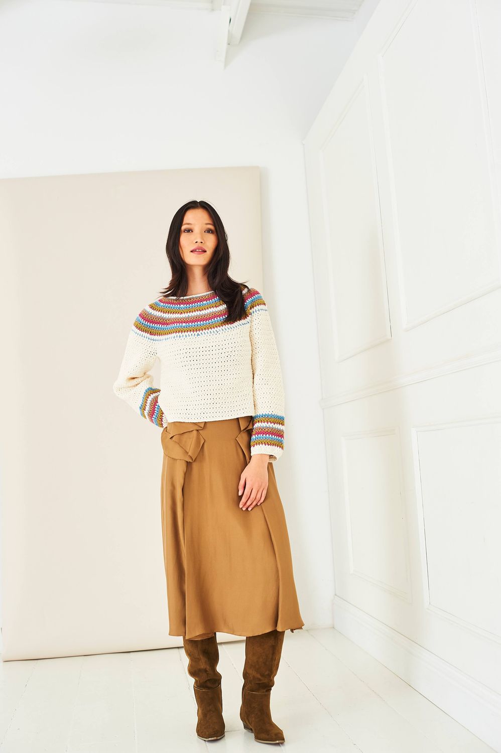 A woman is wearing a cream crocheted sweater with a colourwork yoke and sleeve cuffs.