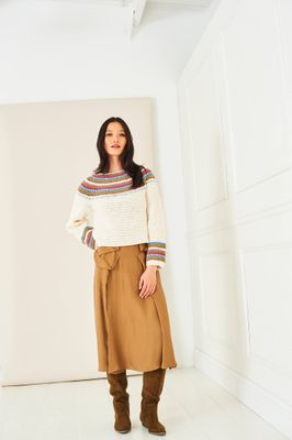 A woman is wearing a cream crocheted sweater with a colourwork yoke and sleeve cuffs.