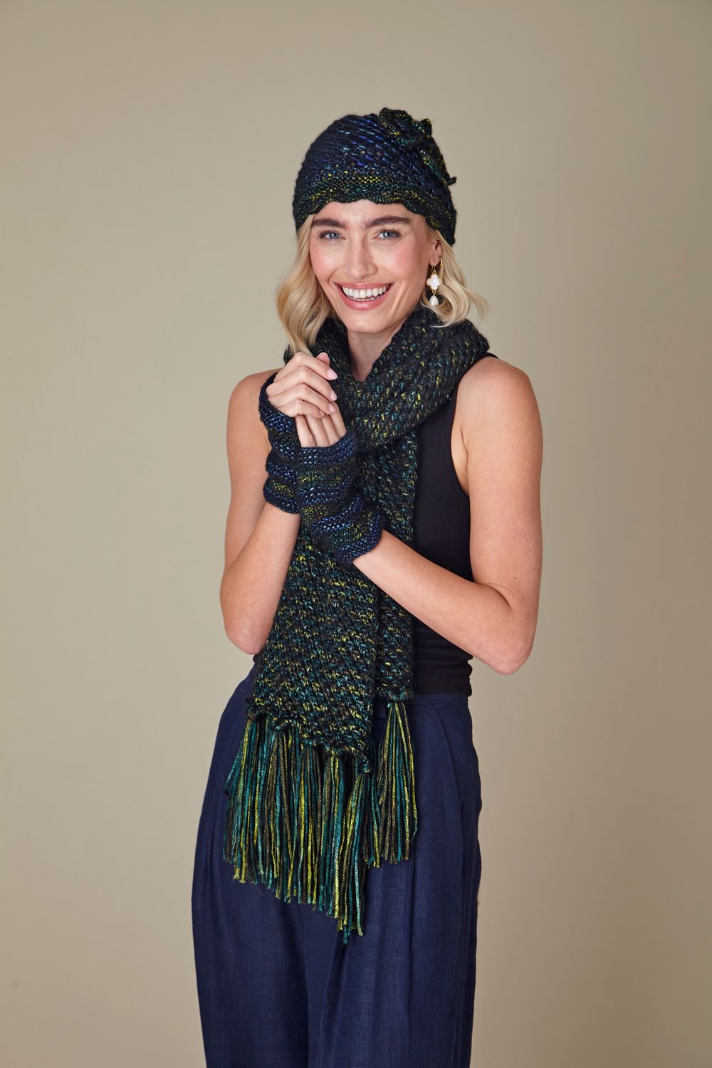 A woman is wearing a dark green knitted hat, scarf and wristwarmers.