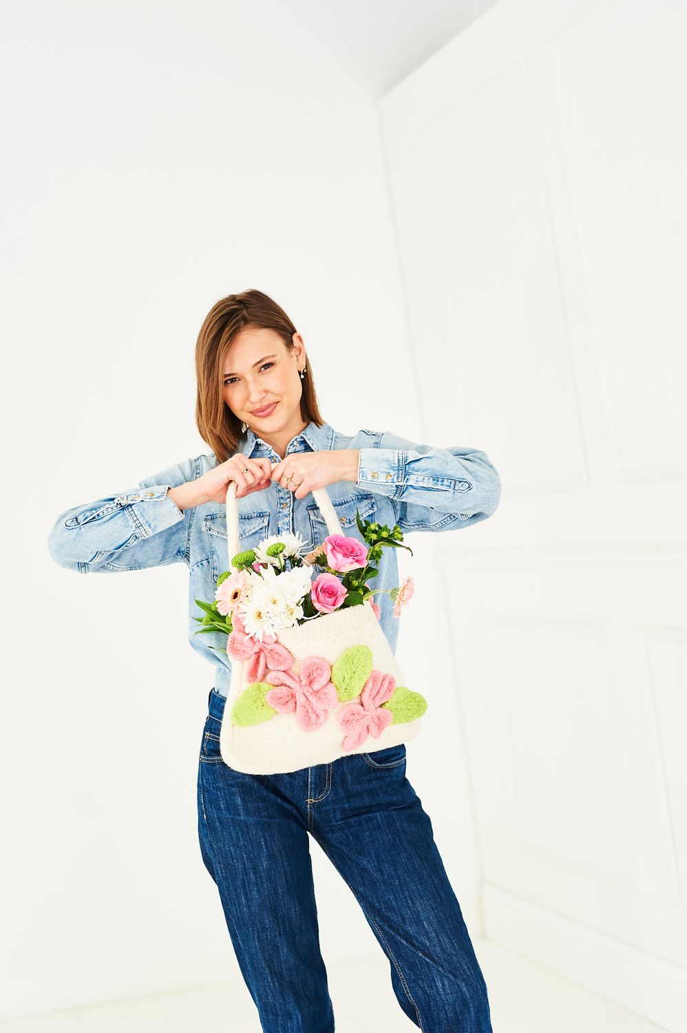 A woman is holding a cream felted knitted bag with pink flower and green leaf motifs. 