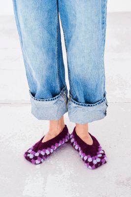 A person wearing a pair of purple felted crochet slippers.