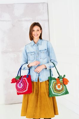 A woman is holding 2 felted crochet bags, one red and one green.