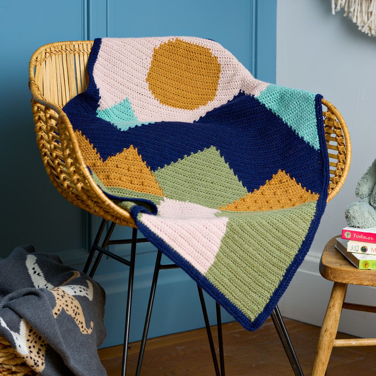 A crocheted blanket with cream, green, yellow and blue colourwork of a landscape.