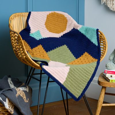 A crocheted blanket with cream, green, yellow and blue colourwork of a landscape.