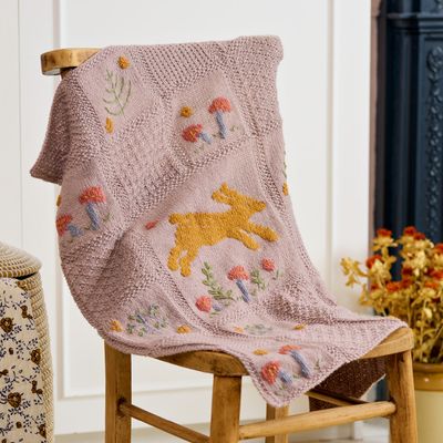 A pale dusky pink knitted blanket with flower and rabbit colourwork motifs.