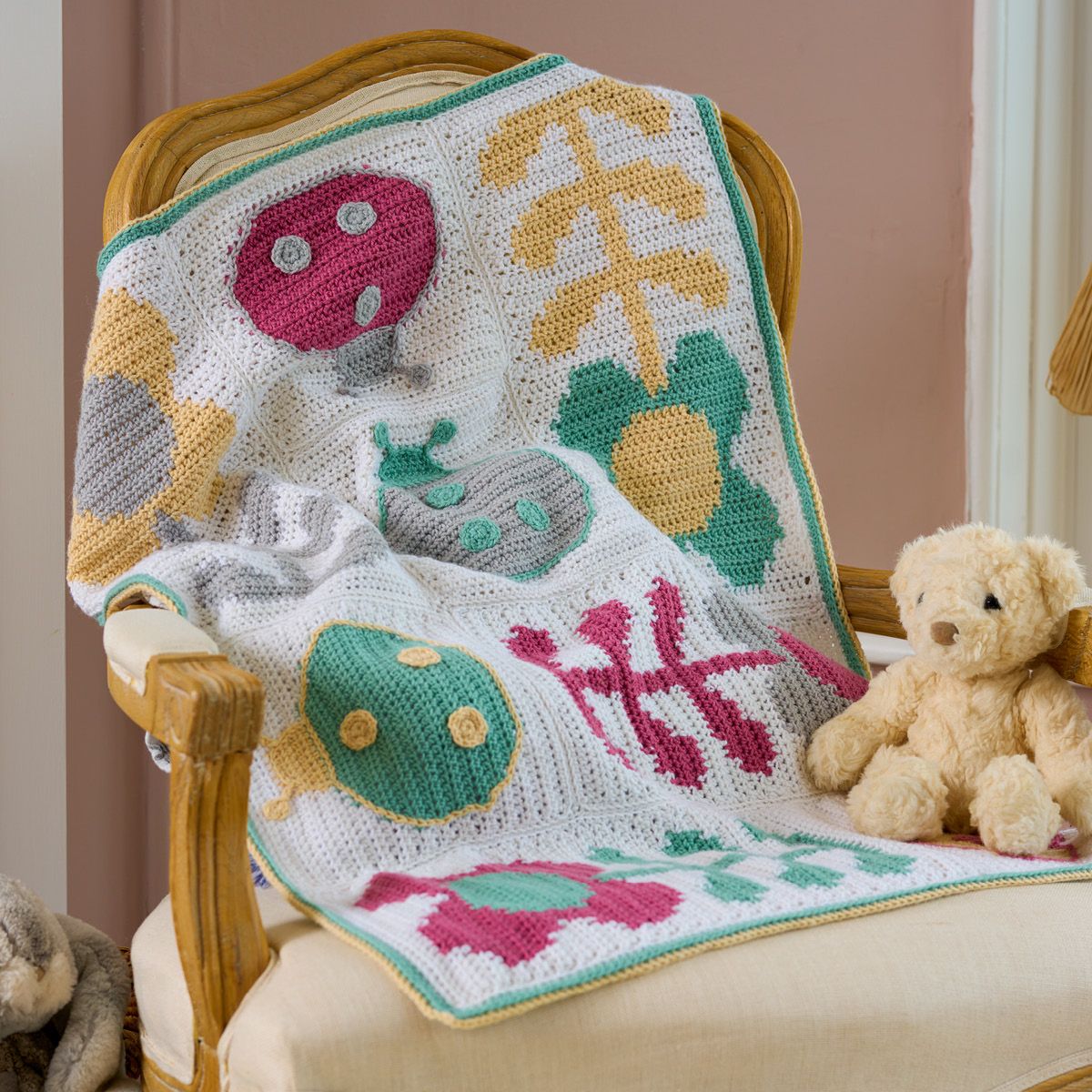 A white crocheted blanket with pink, yellow and green flower and ladybug motifs.