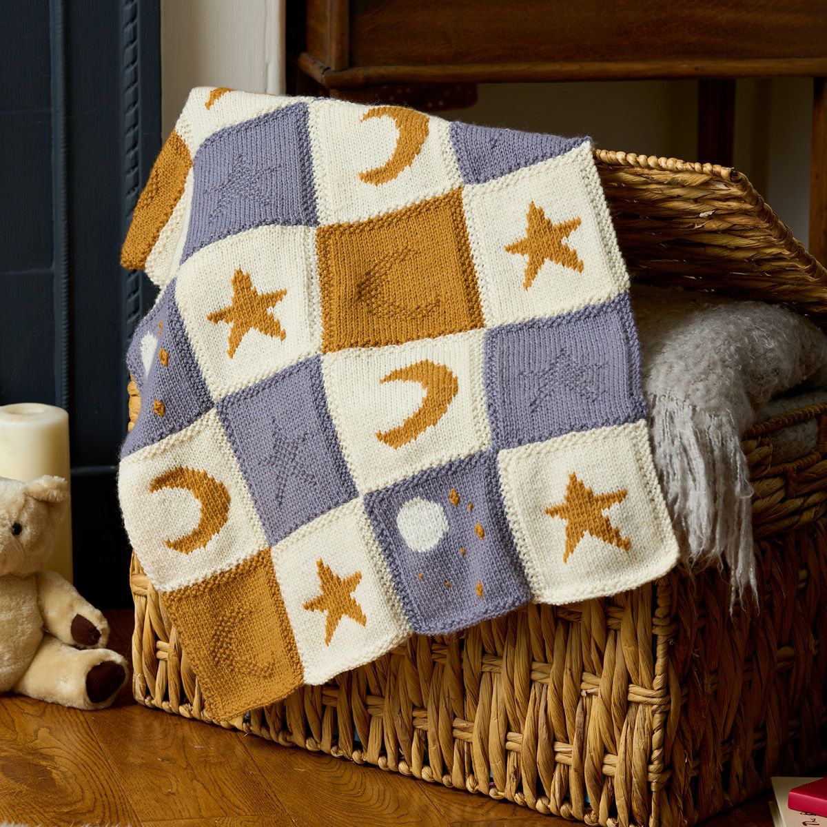 A knitted blanket made up of cream, blue and gold squares with moon and star motifs.