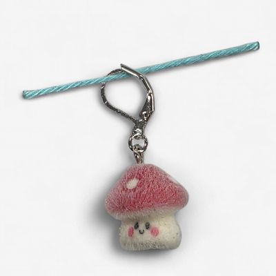A fuzzy red and cream toadstool shaped stitch marker.